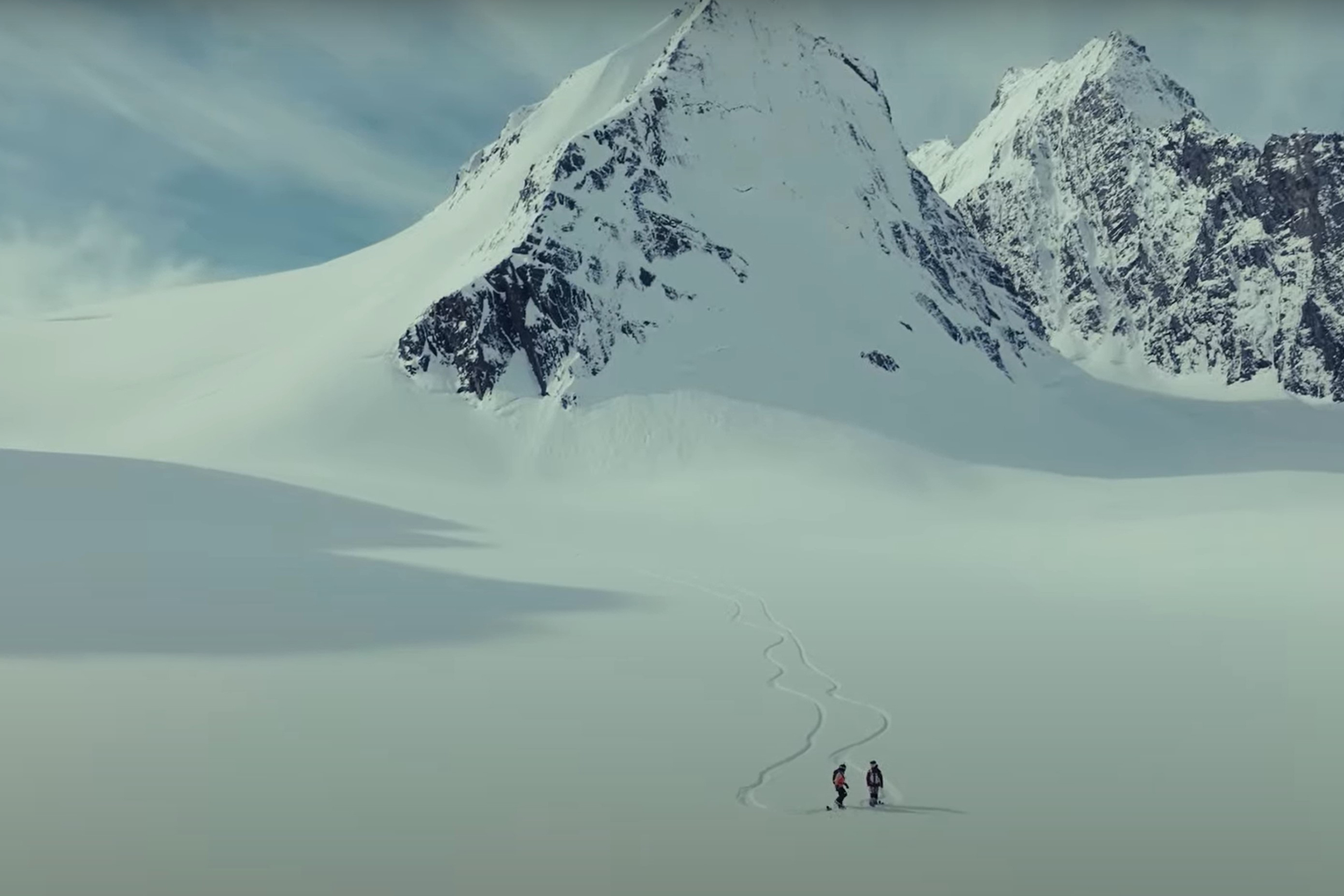 two women are tiny dots against a snowy background with mountains in the background