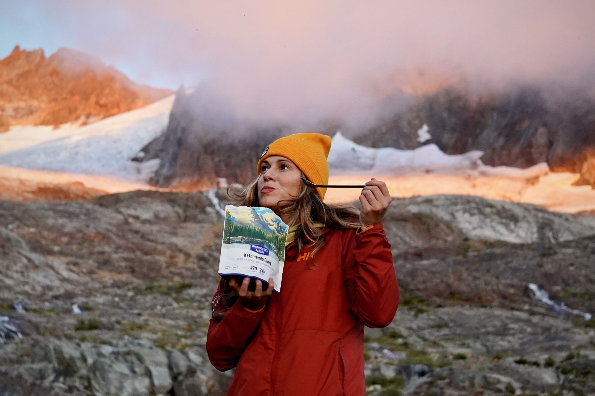 a hiker takes a bite from a kathmandu curry with a mountain and glaciers in the background