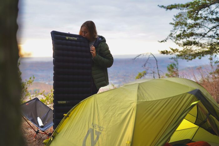 A woman inflates the NEMO Tensor Extreme Conditions in front of a tent.