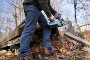 A man cuts wood while wearing work pants.