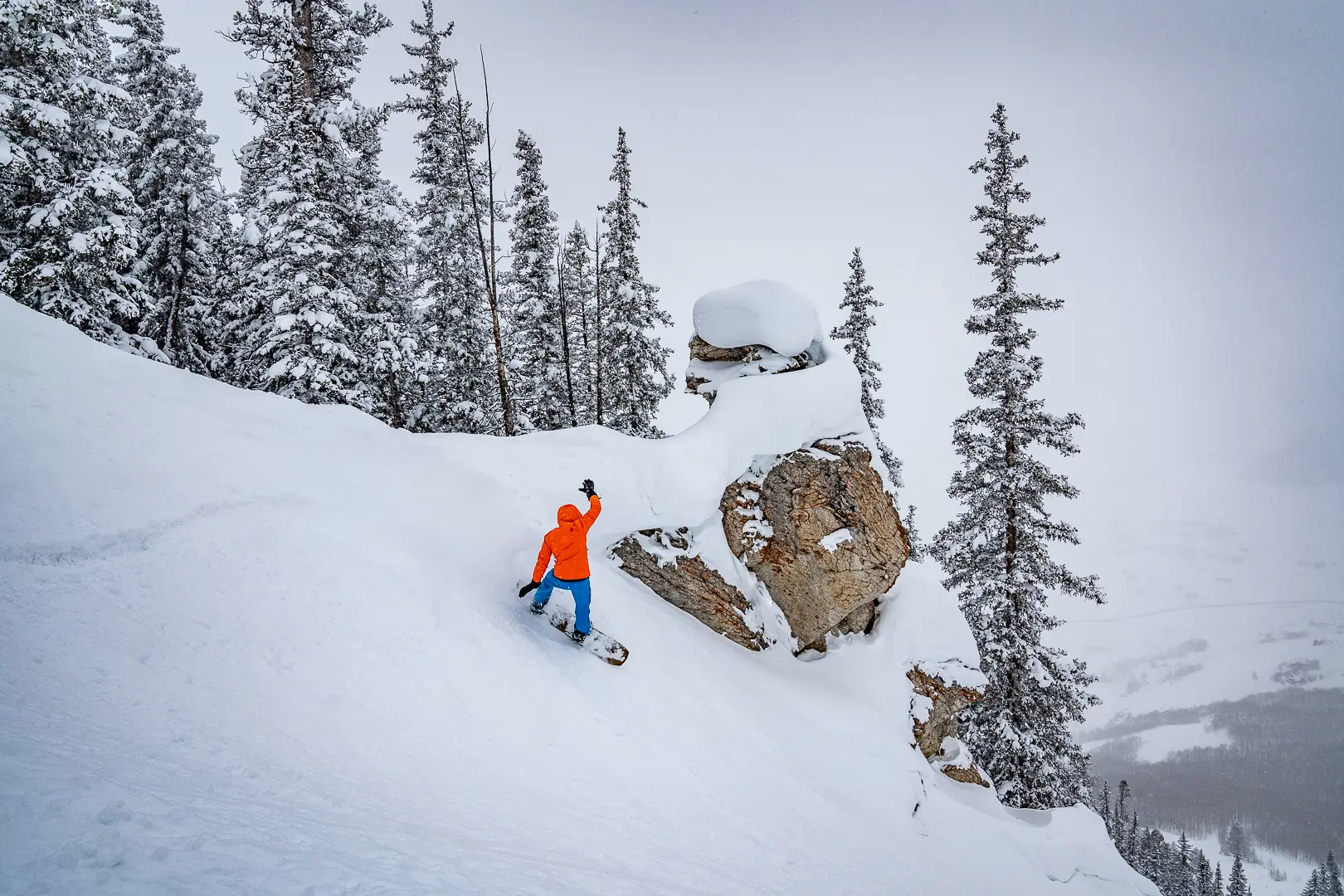 snowboarder taking turn below huge rock outcropping on pow day