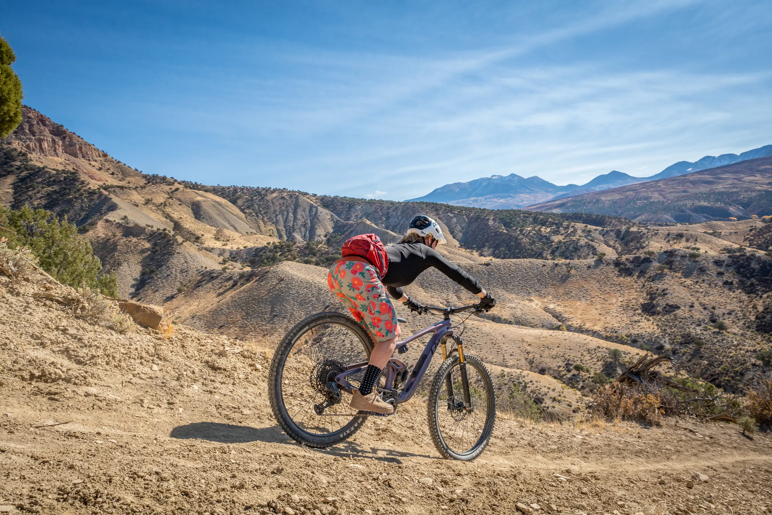 A mountain biker descending a mountain trail wearing colorful women's mountain bike shorts