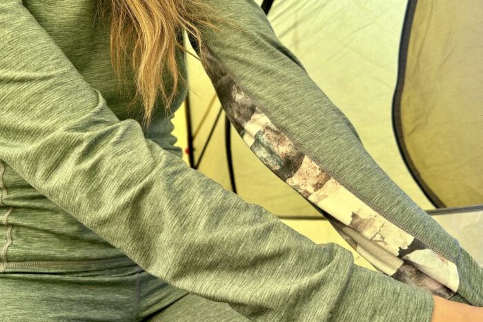 a woman with chest length blonde hair pulling on the sleeves of the Alpine Fit base layer top getting dressed