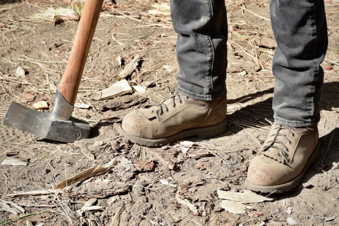 A man demonstrating steel toe work boots while splitting wood with an axe.