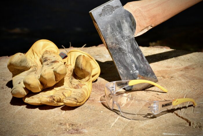 An image showing a pair of leather work gloves and safety glasses as additional equipment for splitting wood with an axe.