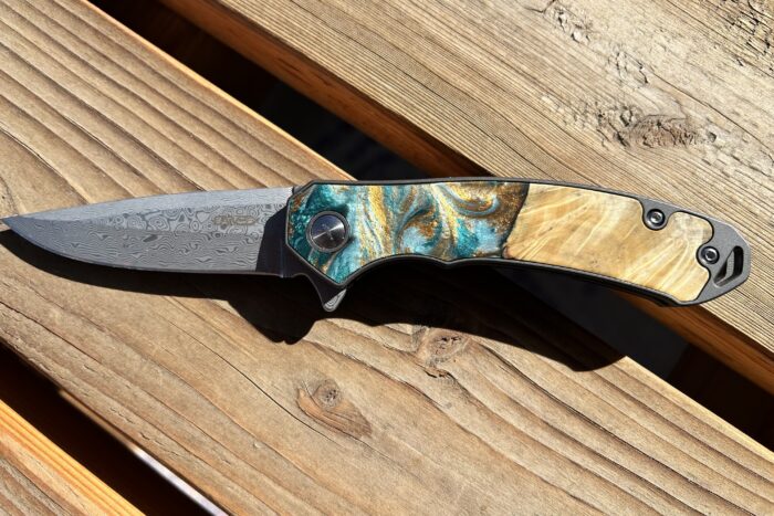 the carved knife with a maple wood grain handle sits on a wood bench outside