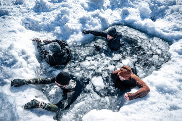 four people try to climb out of a hole in the ice
