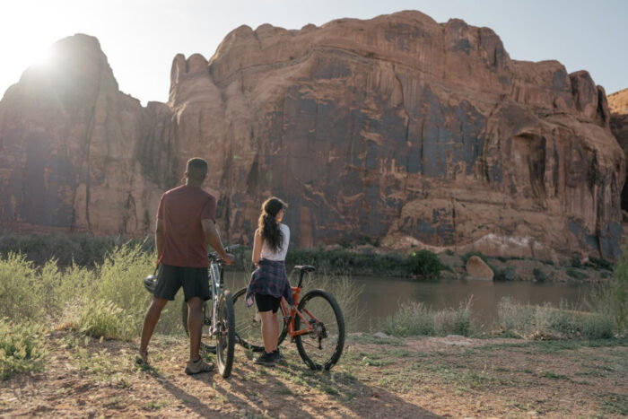 two people stand over mountain bikes looking up at a bluff