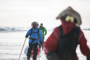 three figures in winter clothing cross-country ski while towing a sled