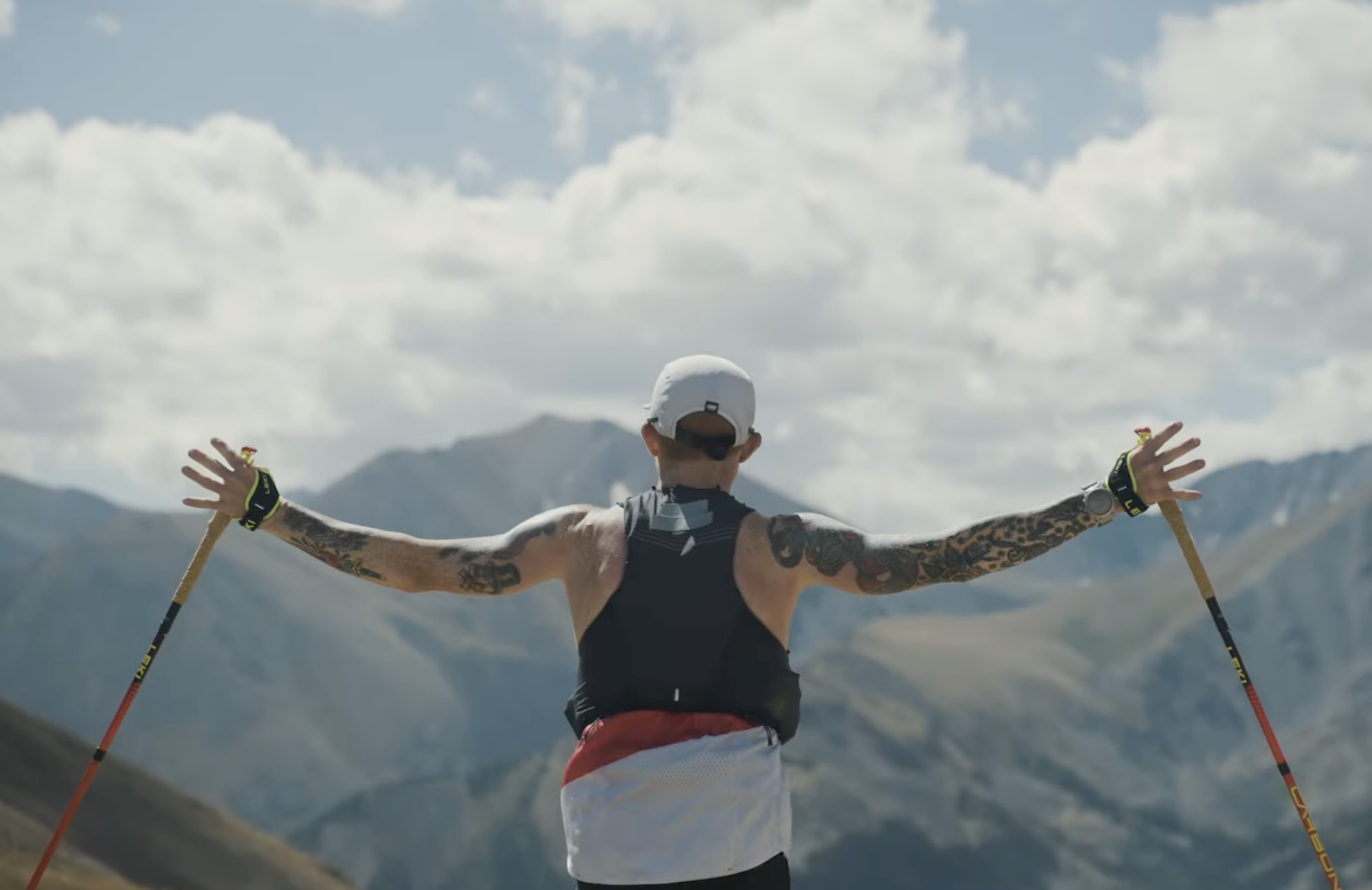 a leadville trail 100 runner with trekking poles throws his arms in the air
