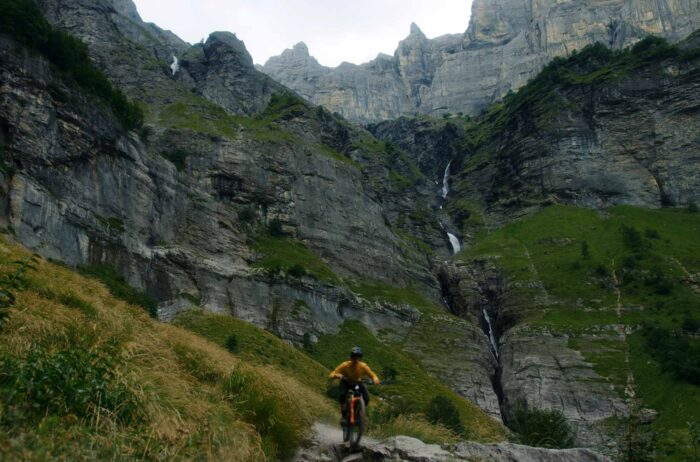 louis citadelle in a yellow long sleeve jersey biking down a rocky trail in the French Alps