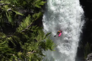 a kayaker in a pink kayaking going down a frothy waterfall