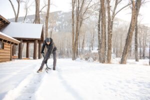 a man shovels snow outside a snowy colorado cabin