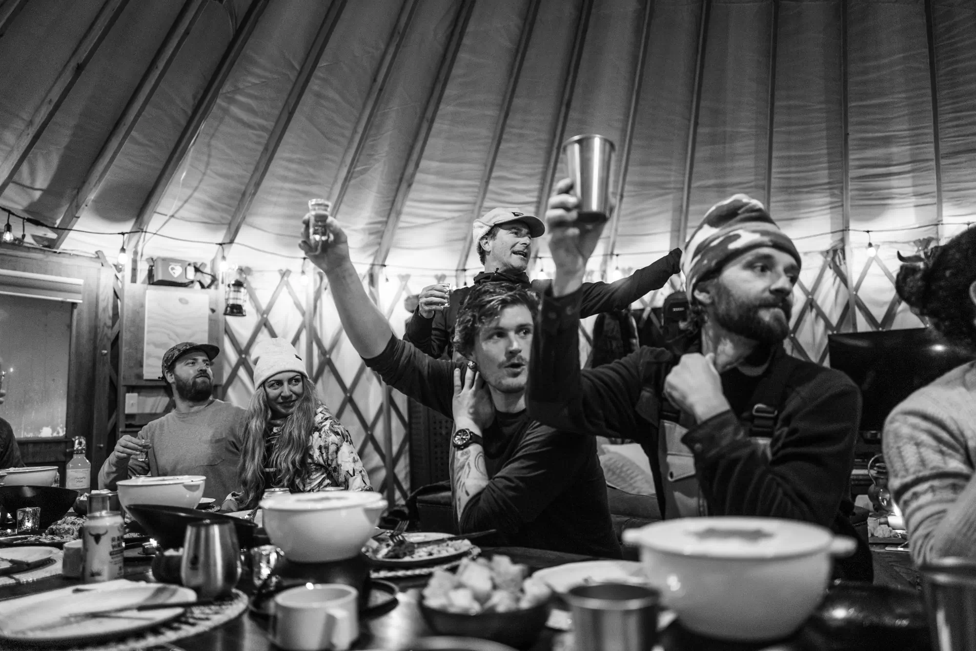 Men hold up drinks while cheering in a yurt