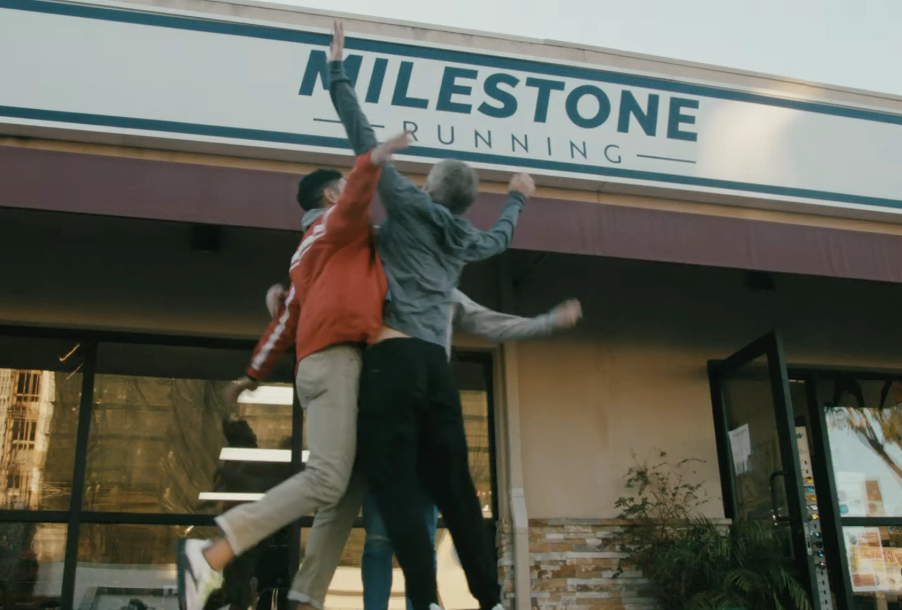Three running store workers jump into air to celebrate in front of the store.