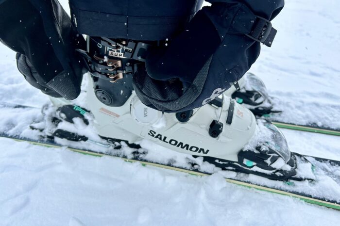two hands with black mitts adjusting the buckles on a white Salomon ski boot