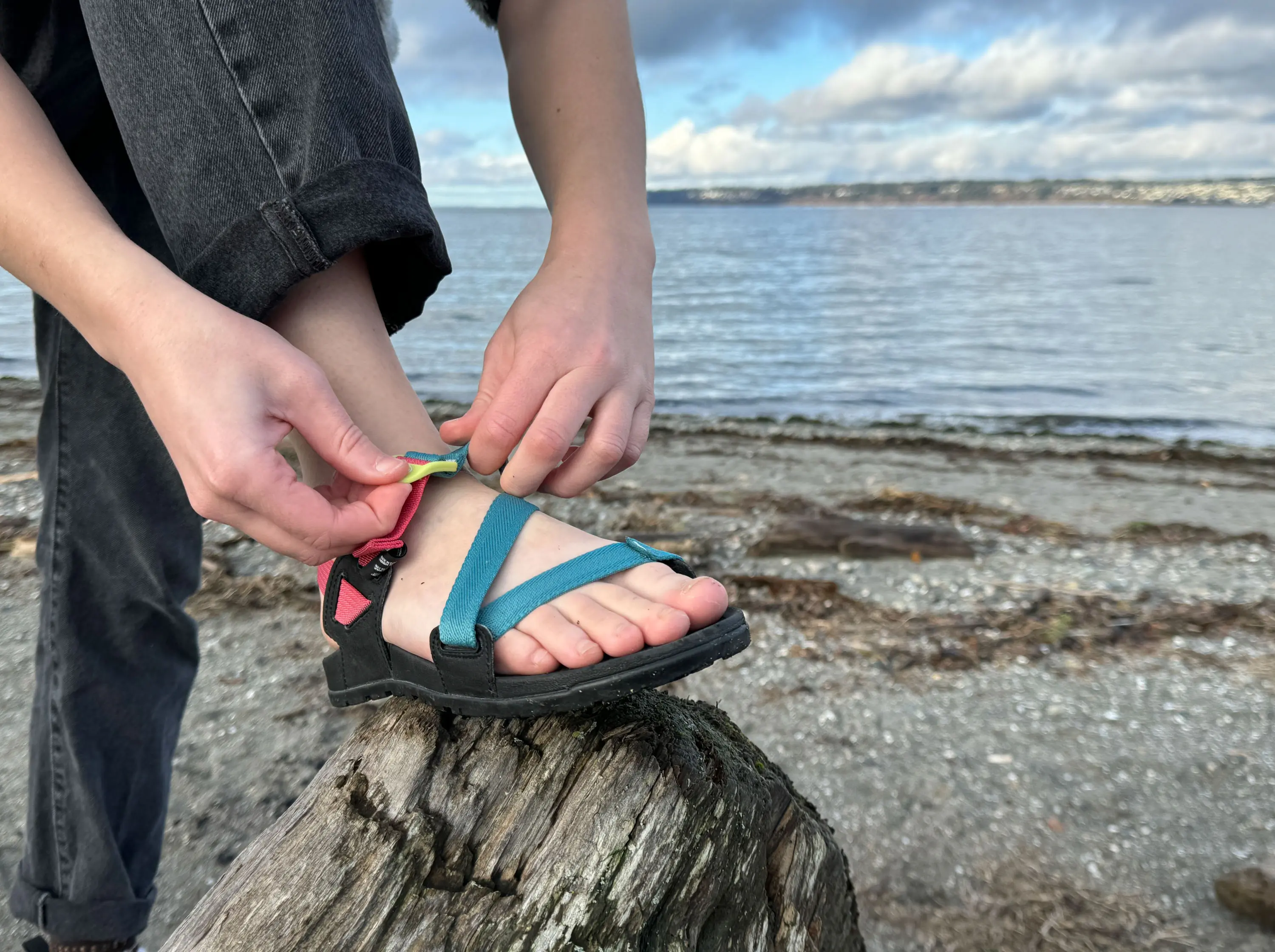 a hiker adjusts the straps of the chaco lowdown sandals on a beach