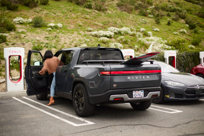 woman charging Rivian truck at Tesla Supercharger