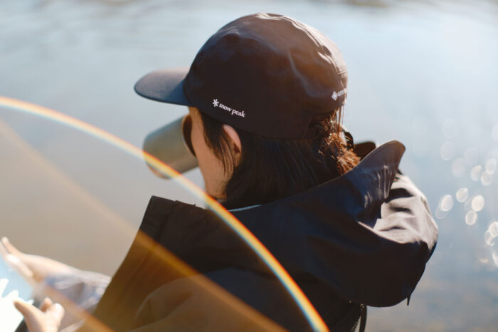 man wearing rain jacket and cap sitting by lake