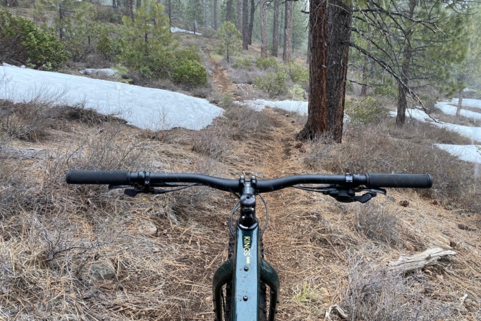 Looking down a trail with snow patches while testing the Ari Kings Peak fat bike