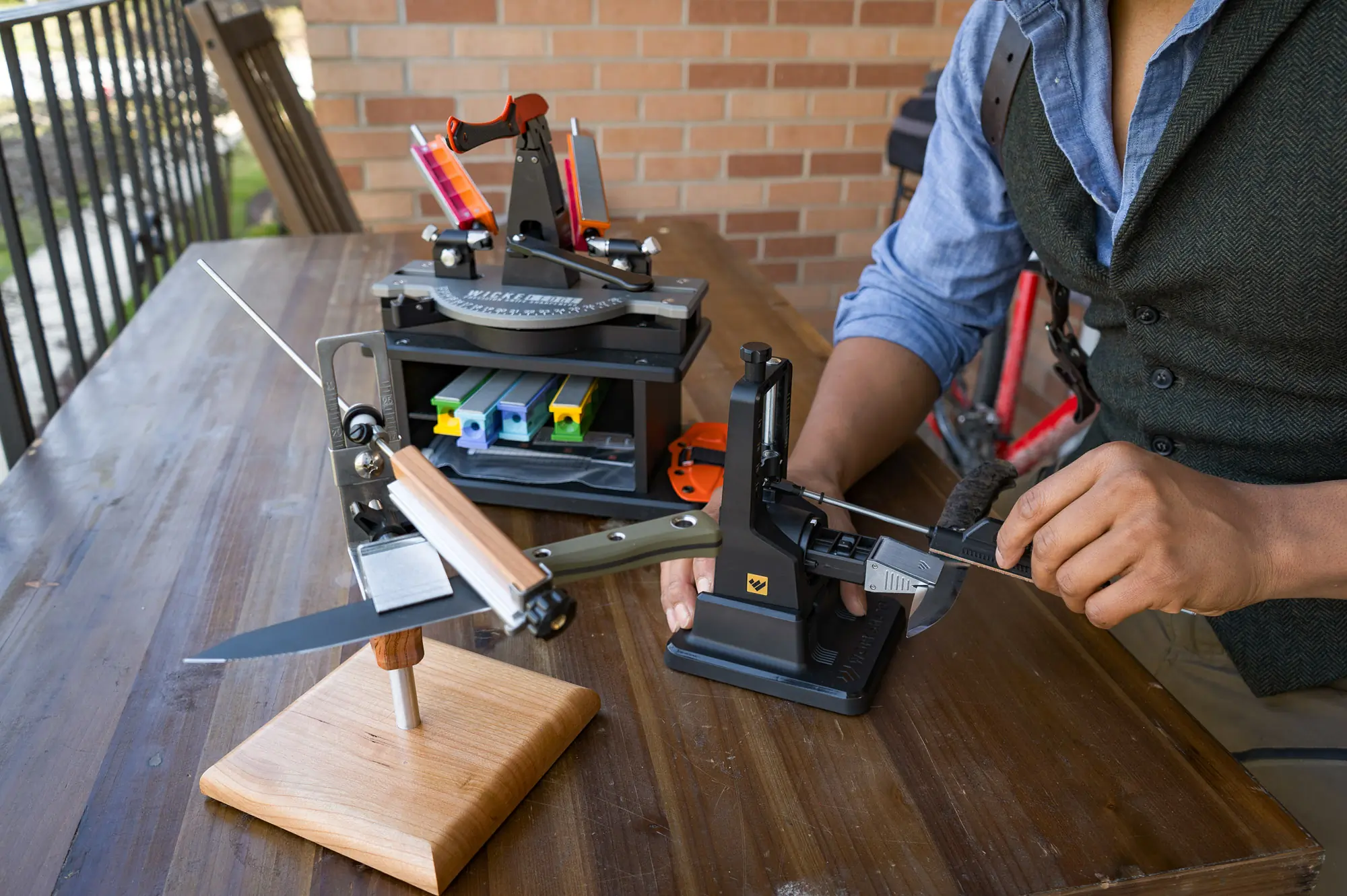 a trio of guided angle sharpeners on a benchtop being used to sharpen various pocket knives