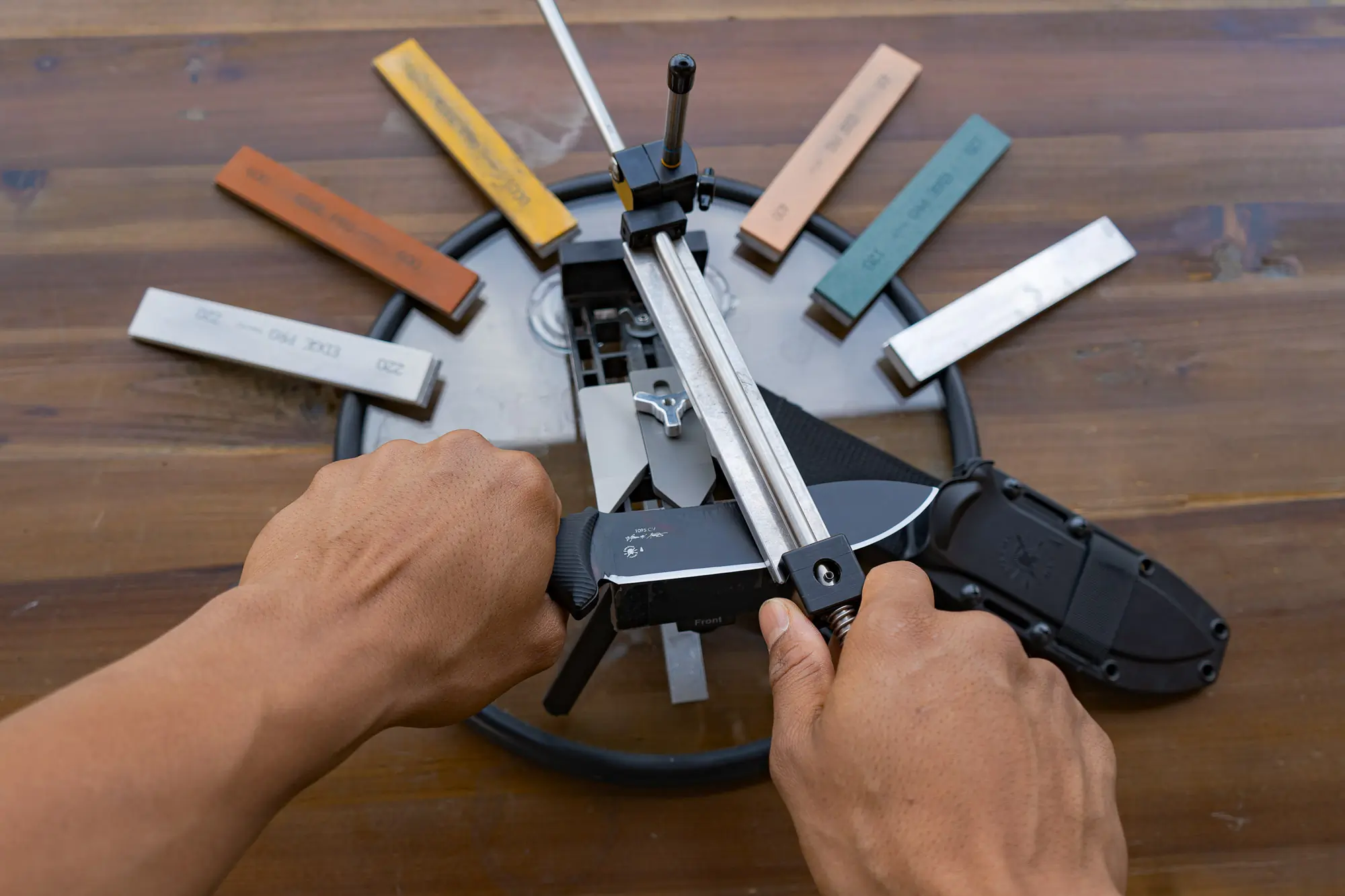 the author using a guided angle style sharpener to touch up an EDC blade, surrounded by different sharpening stones