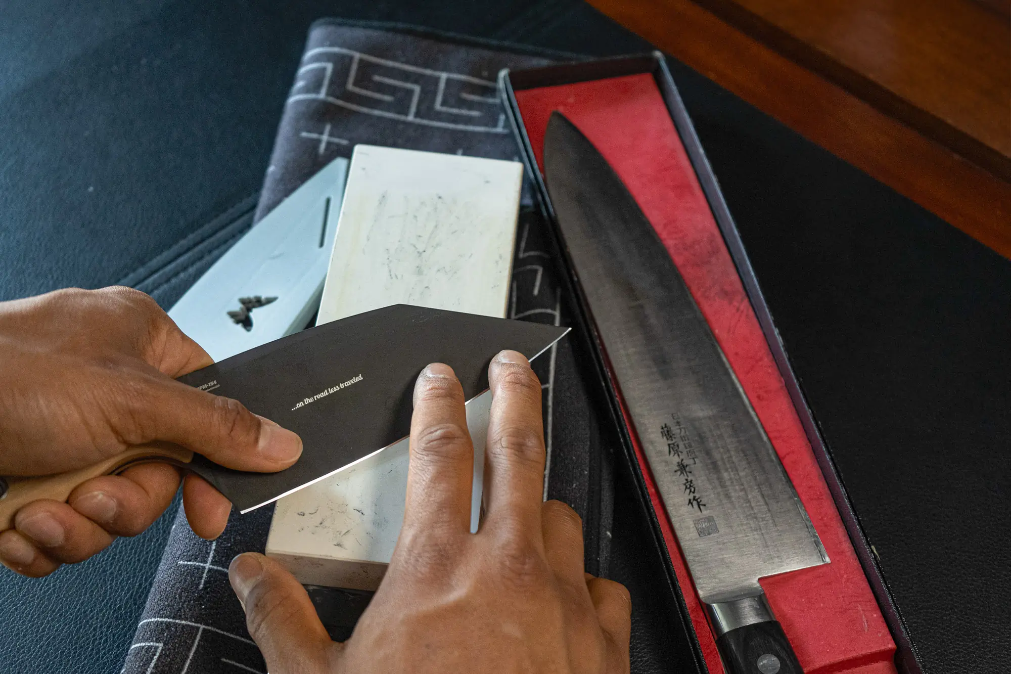 a set of hands pass a large knife across a ceramic whetstone, guiding the angle as it passes