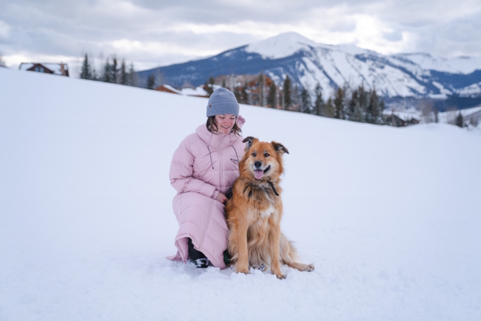 woman kneeling with dog in winter while wearing a parka 