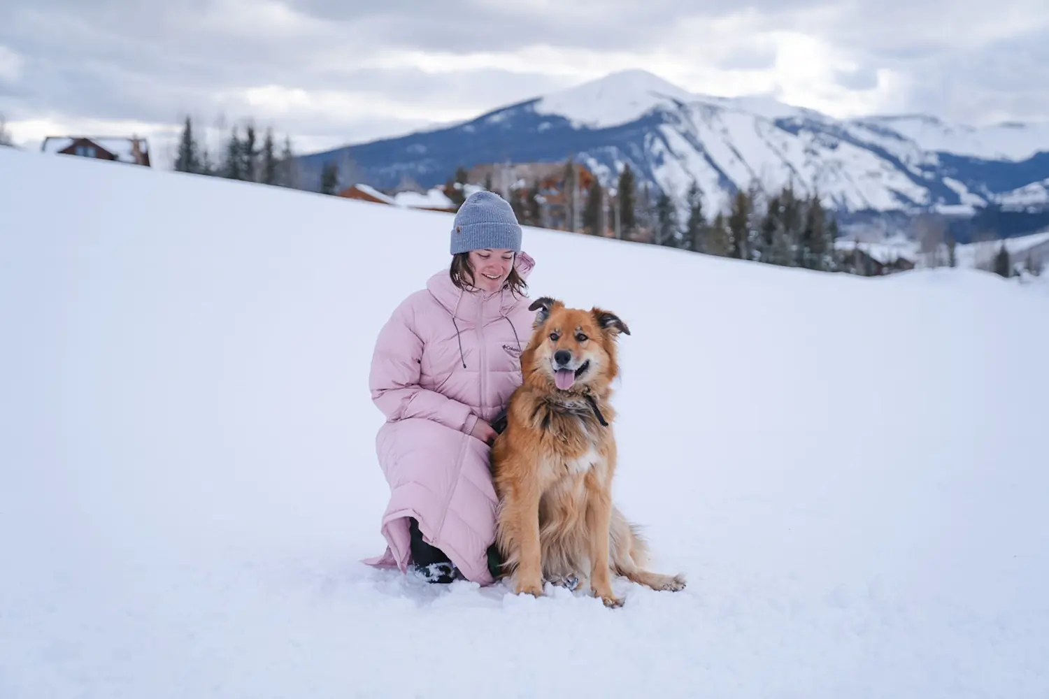 woman kneeling with dog in winter while wearing a parka