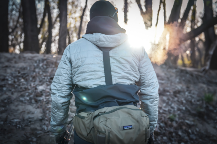 man in patagonia winter fly fishing clothing walking into the sunset in the forest