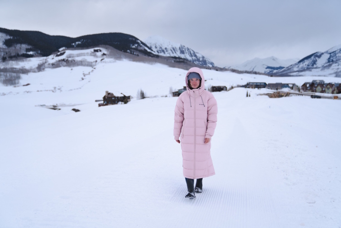 woman walking outside in a wintry mountainous landscape while wearing a long winter coat 