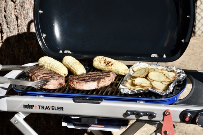 a view of a beautiful steak, corn on the cob, and potato crisp dinner cooking on the Weber Traveler Gas Grill