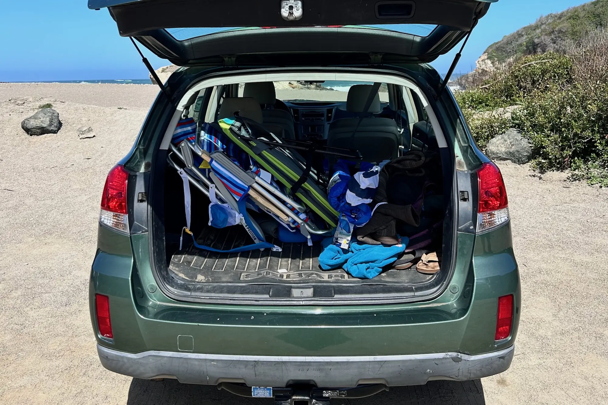 Several beach chairs and a couple of beach umbrellas loaded into the trunk of a Subaru for a day at the beach.