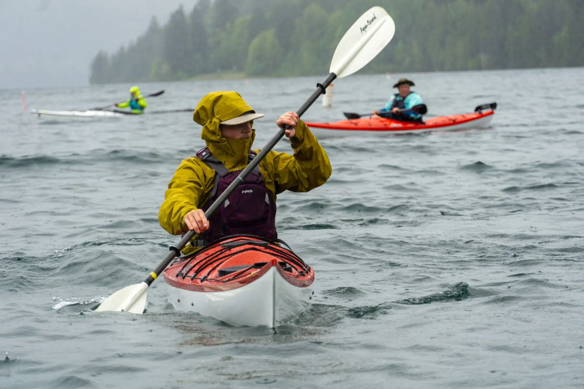 A kayaker in a sea kayak takes a deep stroke while two other kayakers paddled behind him