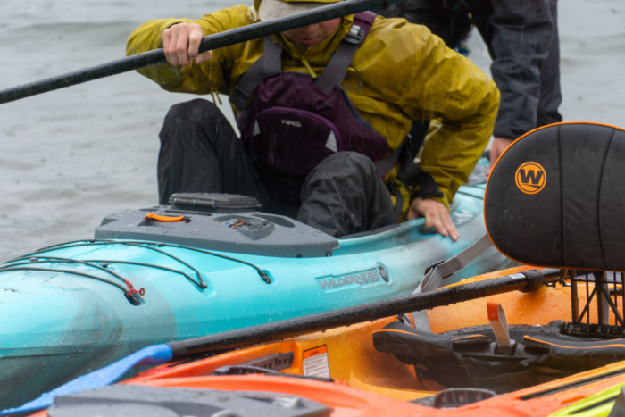 a kayaker sits down into a sit-inside kayak, showing how it requires more flexibility