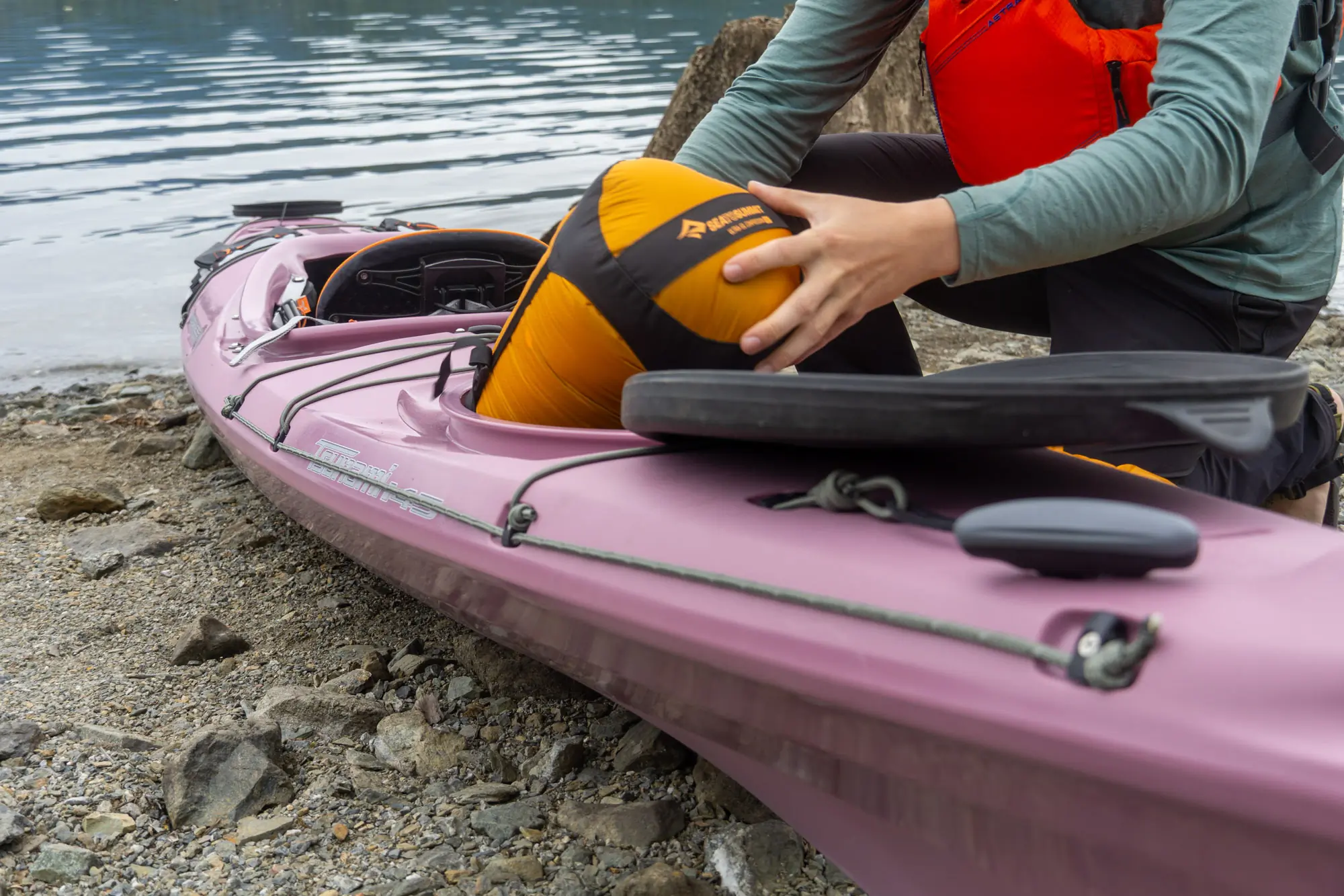 a kayak paddler stashes gear in the rear hatch of a purple touring kayak