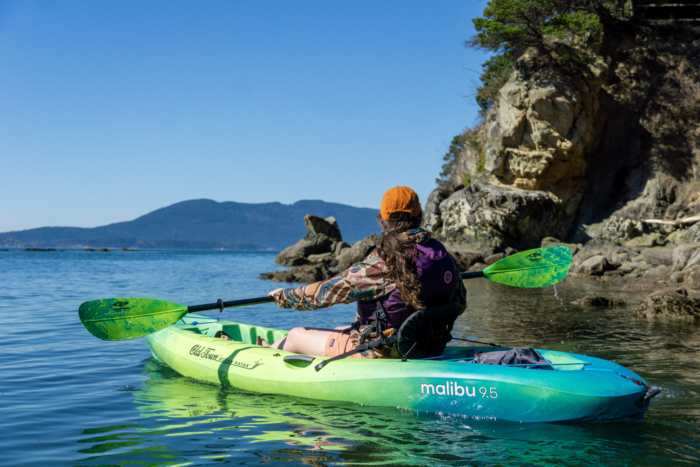 a female kayaker paddles the Old Town Malibu near a rocky shore in Washington