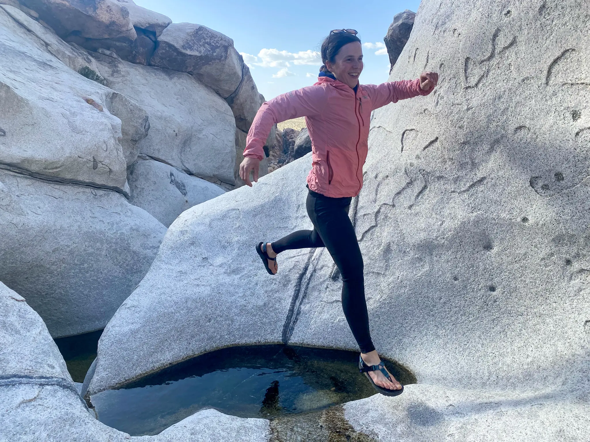 a female hiker makes a leap across water in a slick rock canyon in joshua tree
