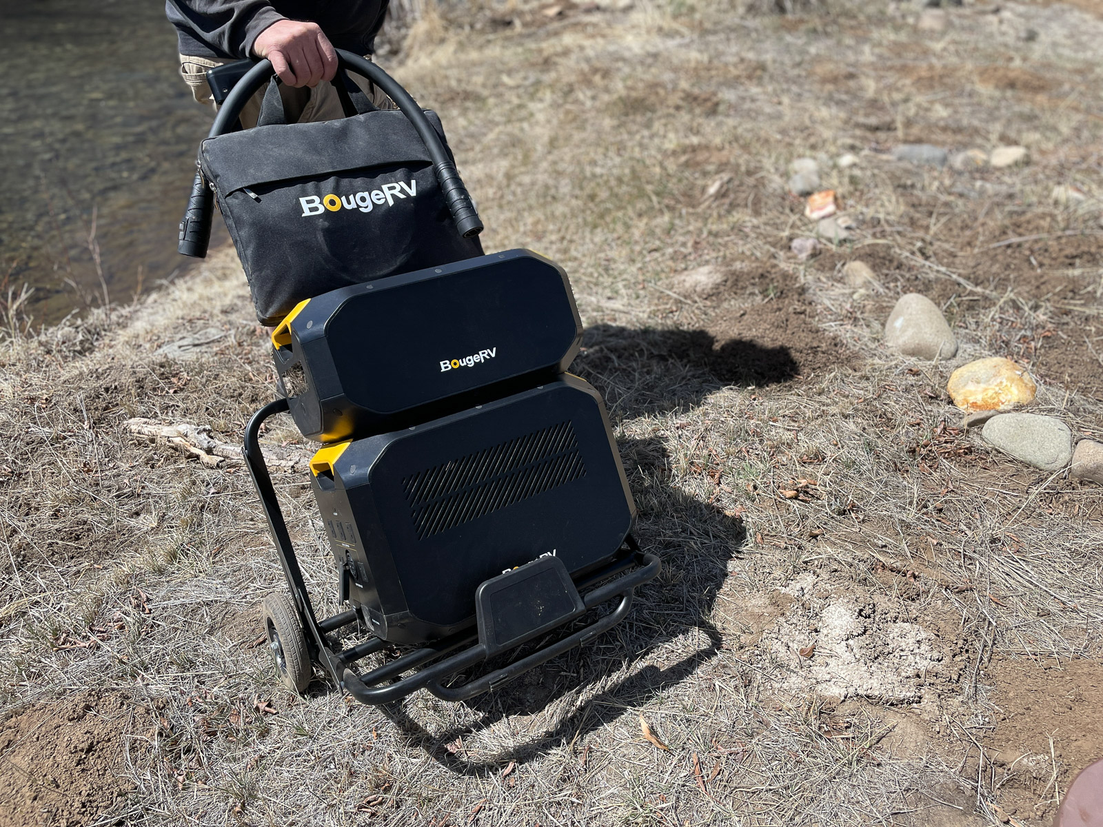 The BougeRV Rover200 power station loaded up on the carrying cart is moved across a dried grass patch