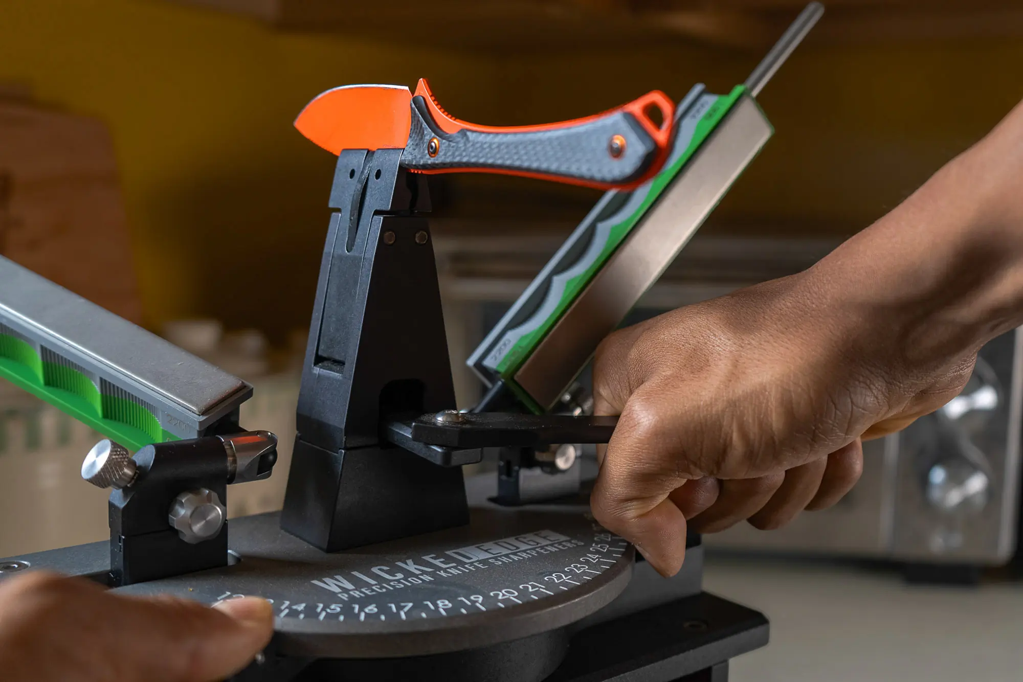 A hand adjusts the clamp of the Wicked Edge Gen 4 Pro Knife Sharpener to hold a knife