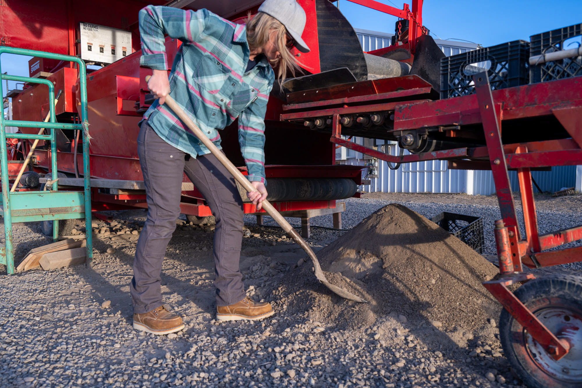 A farmer shovels dirt beneath a machine to sort potatoes