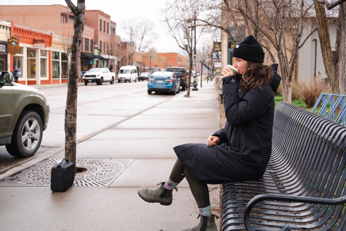 Women sitting on a freshly-rained-on bench wearing a parka. drinking a cup of coffee