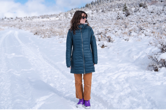 Amid a snow-covered scene, a woman stands tall, wrapped in her KUHL winter jacket