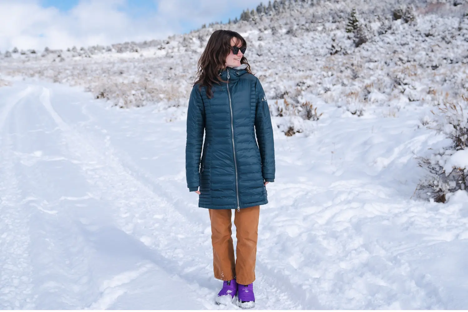Amid a snow-covered scene, a woman stands tall, wrapped in her KUHL winter jacket