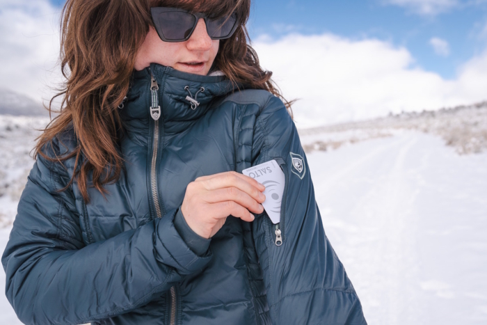 A woman putting a card into the pocket of her KUHL jacket sleeve