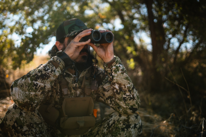 man wearing the ambient 100 hooded jacket while scouting with binoculars