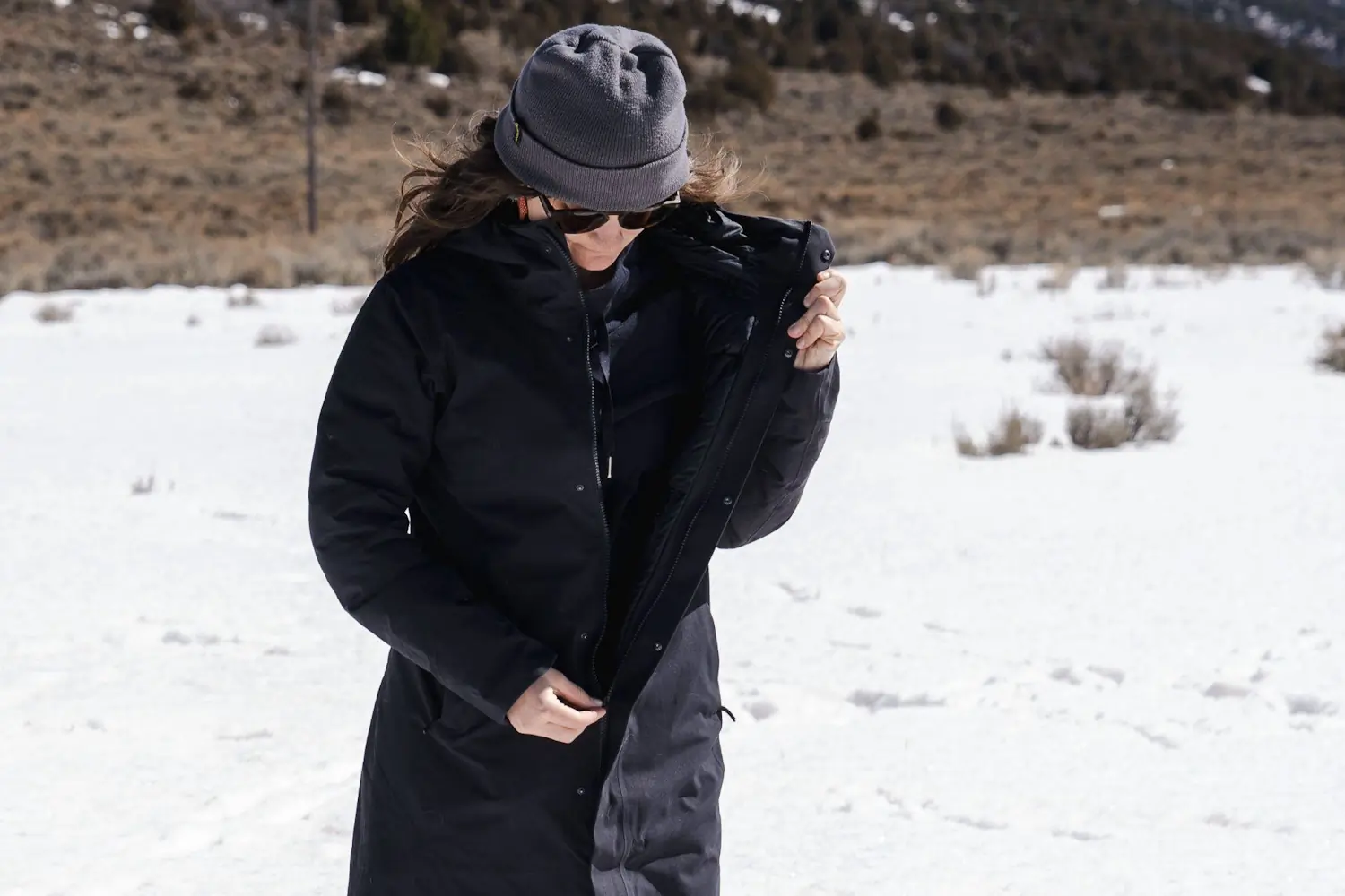 A woman buttoning up her Peter patera parka, in cold windy weathe