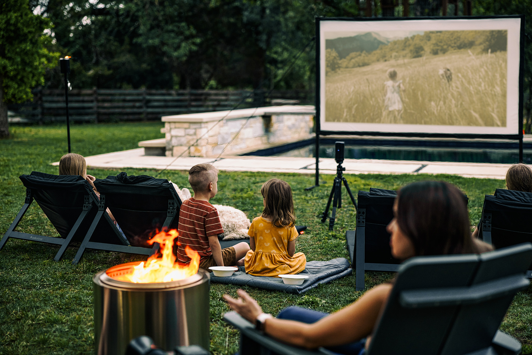 family watching backyard movie next to solo stove fire pit