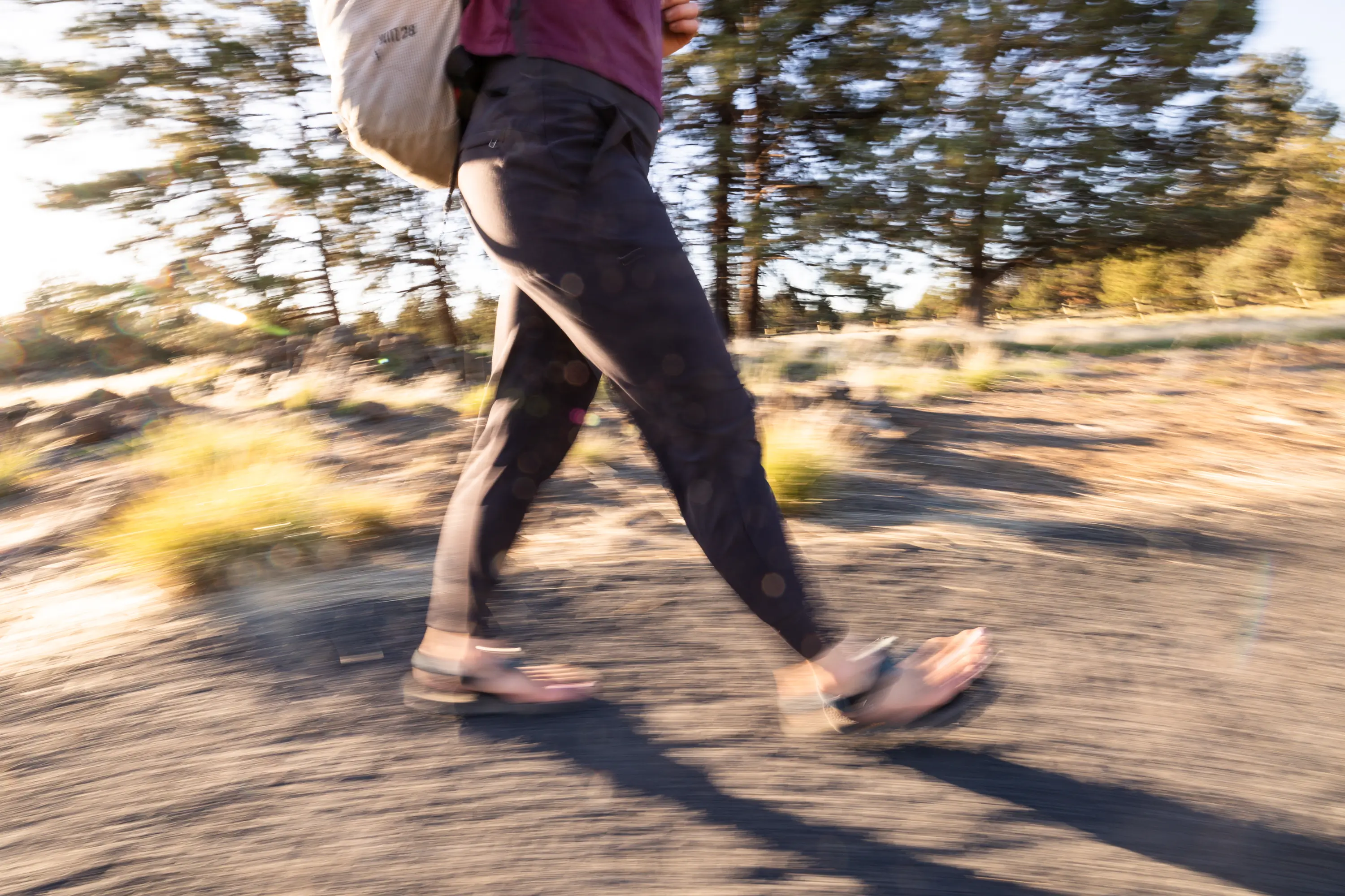 A hiker cuts along a trail in sandals and travel pants