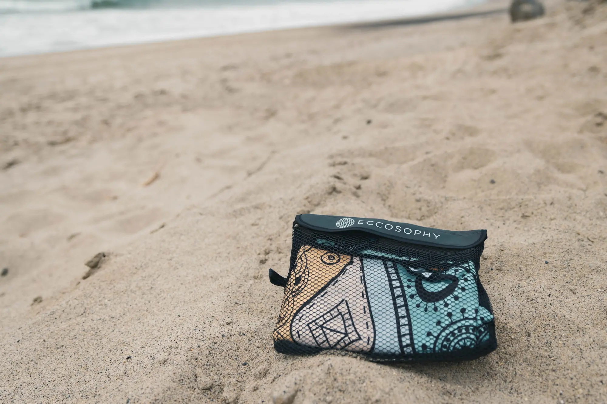 The Eccosophy Microfiber beach towel packed into its mesh carrying bag
